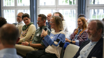 Das Publikum sitzt in Stuhlreihen hintereinander und eine Teilnehmende in der Mitte spricht.  (Bild: ZLE TH Köln)