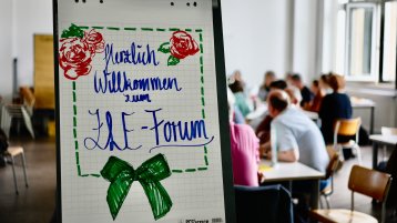 Auf einem weißen Flipchart steht mit blauem Marker ,,Herzlich Willkommen zum ZLE Forum“ geschrieben. Darunter ist eine grüne Schleife. Rechts und links von dem Wort ,,Herzlich“ sind drei rote Rosen mit grünen Blättern. Die Schrift ist mit grünen Strichen umrahmt. (Bild: ZLE TH Köln) Auf einem weißen Flipchart steht mit blauem Marker ,,Herzlich Willkommen zum ZLE Forum“ geschrieben. Darunter ist eine grüne Schleife. Rechts und links von dem Wort ,,Herzlich“ sind drei rote Rosen mit grünen Blättern. Die Schrift ist mit grünen Strichen umrahmt. (Bild: ZLE TH Köln)
