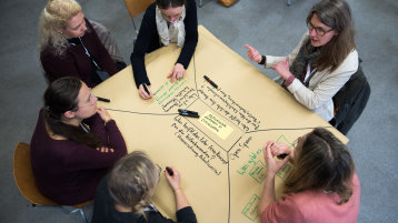 Foto: Mehrere Personen diskutieren an einem Tisch mit Brownpaper die aktivierende Online-Lehre (Bild: Costa Belibasakis)