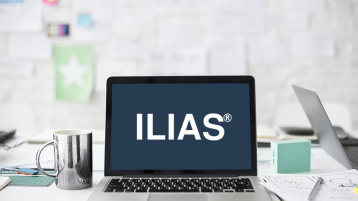 Ein silberner Laptop auf dem das Logo der Firma ILIAS zu sehen ist, im Hintergrund ein Arbeitsplatz (Bild: Medienbüro ZLE)