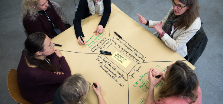 Foto: Mehrere Personen diskutieren an einem Tisch mit Brownpaper die aktivierende Online-Lehre (Bild: Costa Belibasakis)