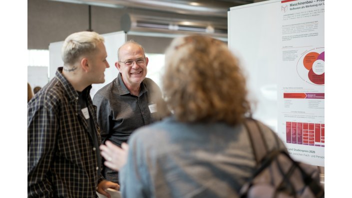Foto: Drei Personen unterhalten sich vor einem Forschungsposter mit Diagrammen und Texten.