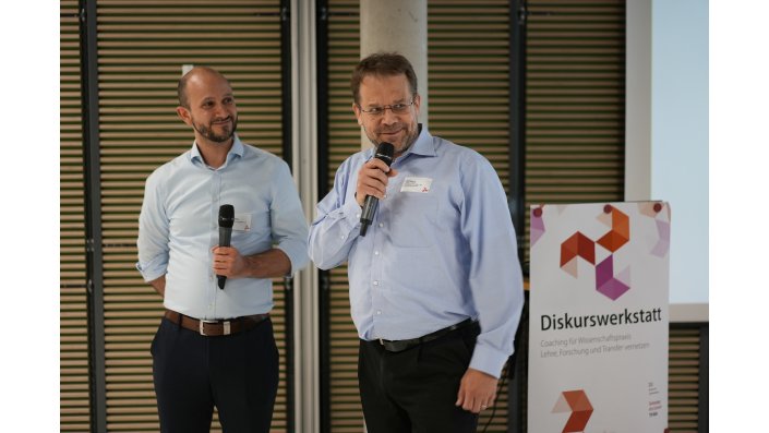 Prof. Dr. Jan Kukulies und Prof. Dr. Ingo Wieck stehen links neben der Leinwand und Prof. Wieck spricht. 