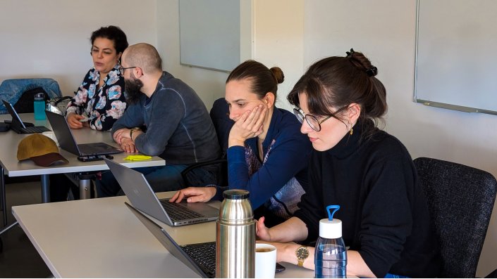 Mitglieder der CoE arbeiten an ihren Laptops und unterhalten sich.