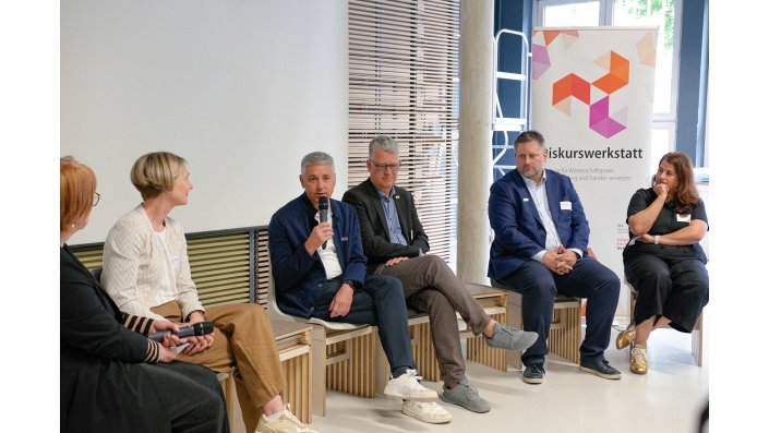 Dr. Birgit Szczyrba, Prof. Dr. Sylvia Heuchemer, Prof. Dr. Axel Faßbender, Prof. Dr. Matthias Hochgürtel, Prof. Dr. Christian Wolf und Joelle Coutinho sitzen in einer Reihe und Prof. Faßbender spricht. 