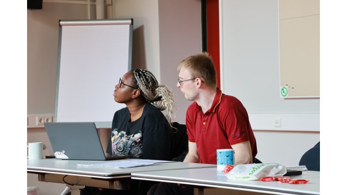 Fabian Hesterberg und seine Arbeitsassistenz sitzen an einem Tisch und präsentieren einen Vortrag zum Arbeitsbereich „EiN* Ort für inklusives Wissen“. 