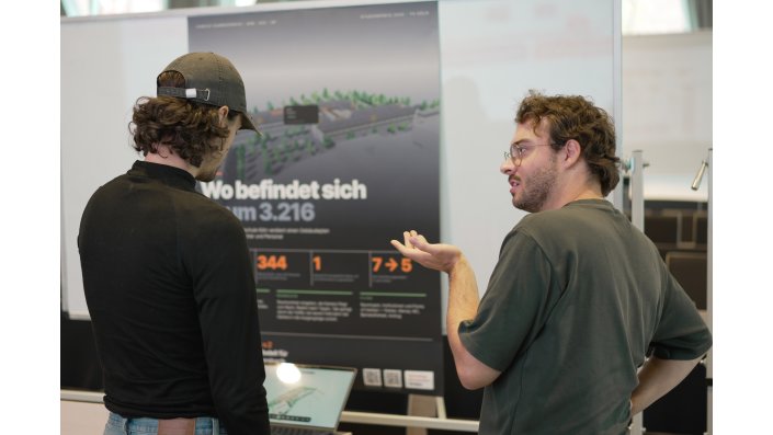 Foto: Zwei Männer stehen vor einem Forschungsposter und unterhalten sich.