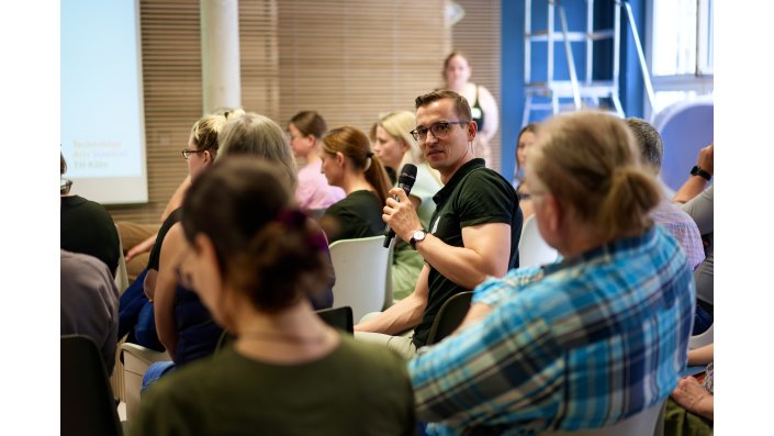 Ein Mann mit Brille sitzt im Publikum und spricht in ein Mikrofon. 