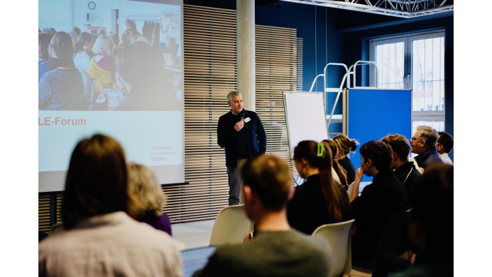 Prof. Dr. Axel Faßbender steht vor einer Leinwand und vor ihm sitzen die Teilnehmenden.