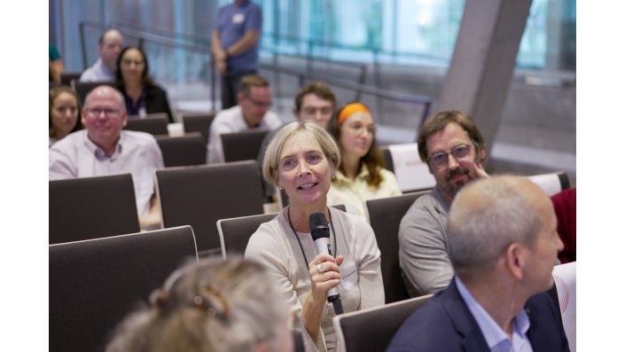 Foto: Eine Frau aus dem Publikum spricht in ein Mikrofon. 