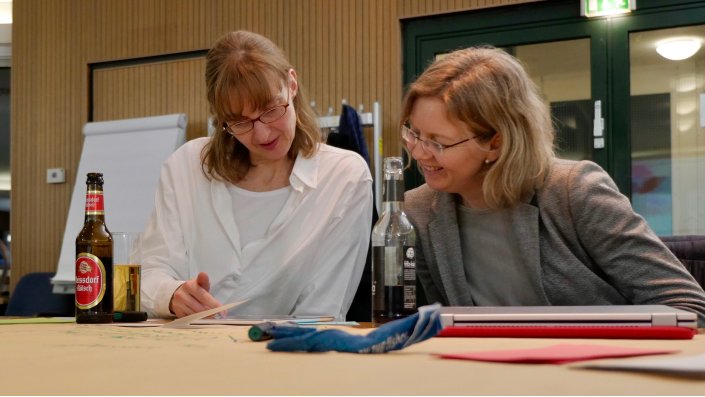 Foto: Zwei Teilnehmende am Tablet, davor Brownpaper mit Stift und Notizen