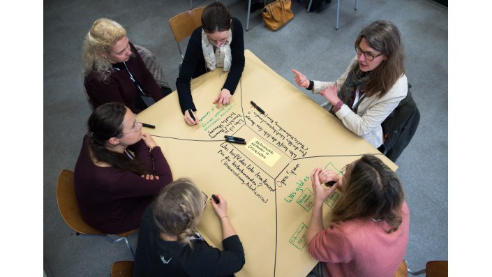Foto: Mehrere Personen diskutieren an einem Tisch mit Brownpaper die aktivierende Online-Lehre
