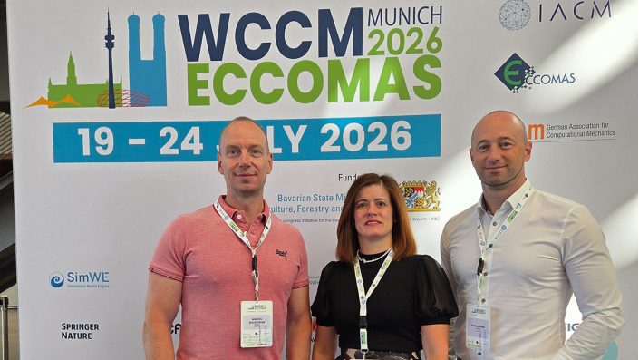 [Foto] Eine Frau und zwei Männer vor einem Plakat mit Logos und dem Titel des Symposiums