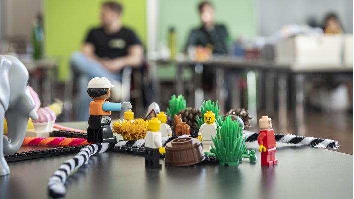 Legofiguren auf einem Tisch, im Hintergrund Menschen