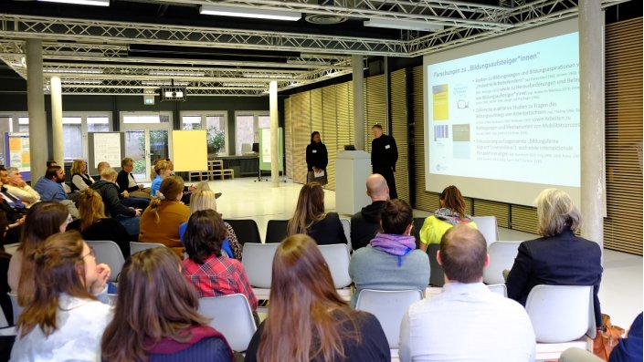 zwei Personen neben Projektion einer Präsentation vor Publikum