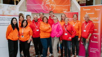 Kolleg*innen des Referats Internationale Angelegenheiten stehen in rot-, orange- und pinkfarbenen Pullovern vor Roll-Ups.  (Bild: TH Köln / Kim Strumpf)