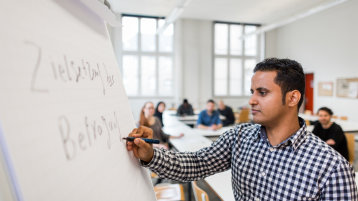Ein Student schreibt auf eine Flipchart, im Hintergrund sind undeutlich weitere Studierende zu erkennen.  (Bild: Thilo Schmülgen/TH Köln)