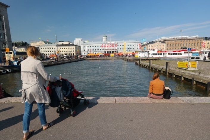 Mutter geht mit Kind im Kinderwagen bei sonnigem Wetter in Helsinki spazieren.