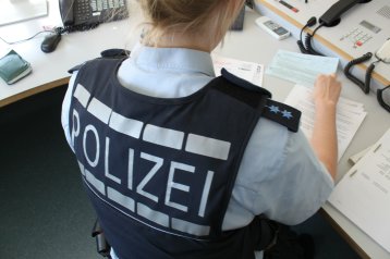Polizistin sitzt mit dem Rücken zur Kamera am Schreibtisch und blickt auf Dokumente