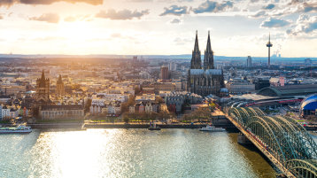 Man sieht Köln bei Tageslicht von oben, der Dom prominent in der Mitte, die Hohenzollernbrücke und angrenzende Gebiete. (Bild: Adobe Stock / Simon)