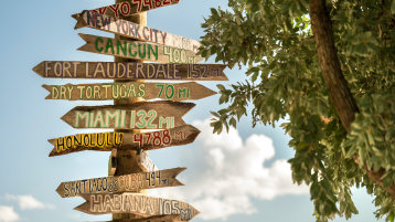 Man sieht einen Wegweiser, der in ganz verschiedene Richtungen unterschiedliche internationale Städte mit Kilometerangabe ausweist.  (Bild: Adobe Stock / Cavan)
