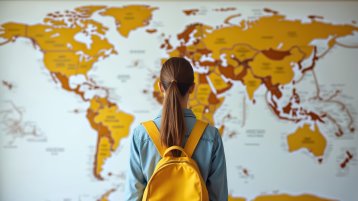 Eine Frau mit gelbem Rucksack steht vor einer gelb eingefärbten Weltkarte.  (Image: Adobe Stock / miss irine)