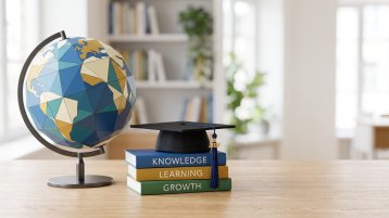 Schematischer Globus mit danebenliegenden Büchern und Studienmütze (Bild: AdobeStock_2126363902_Chrish)
