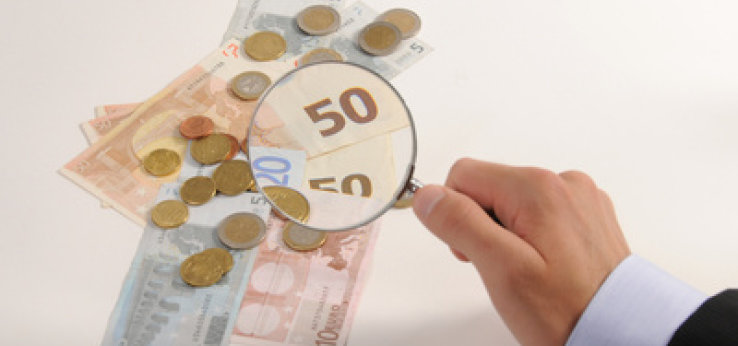 Eine Lupe vergrößert Münzen und Geldscheine (Bild: Jorma Bork / pixelio.de)