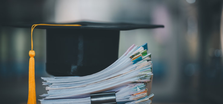 Graduation cap lays on a pile of papers at the desk,concept education for work  (Bild: Adobe Stock / mnirat)