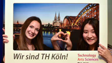 Zwei Studentinnen halten einen Rahmen mit der Aufschrift "Wir sind TH Köln!". Sie formen mit ihren Händen ein Herz. Im Hintergrund sieht man den Dom und die Hohenzollernbrücke. (Bild: Costa Belibasakis, TH Köln) Zwei Studentinnen halten einen Rahmen mit der Aufschrift "Wir sind TH Köln!". Sie formen mit ihren Händen ein Herz. Im Hintergrund sieht man den Dom und die Hohenzollernbrücke. (Bild: Costa Belibasakis, TH Köln)