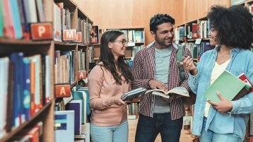 Drei Studierende unterhalten sich in der Bibliothek (Bild: iStock)