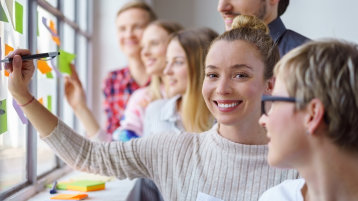 Workshopteilnehmende arbeiten zusammen und schreiben auf Zettel am Fenster (Bild: Adobe Stock)