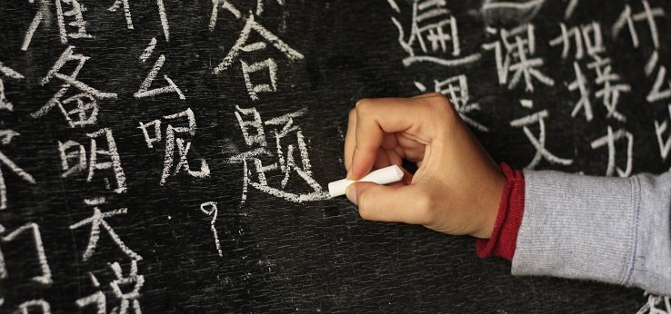 Person schreibt chinesische Zeichen auf eine Tafel (Bild: f.ield_of_vision/iStock.com)