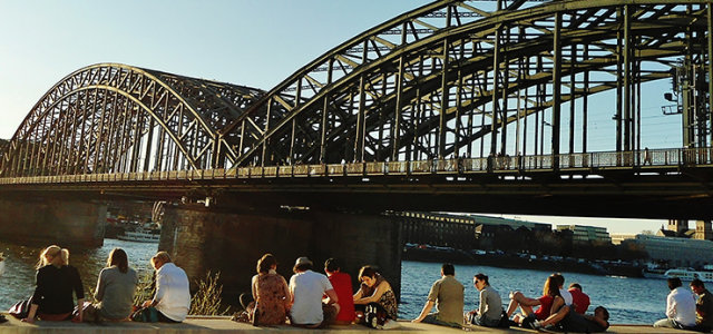 Studierende sitzen am Rhein auf der Deutzer Seite mit Blick auf die Hohenzollernbrücke und den Kölner Dom (Bild:TH Köln / Damir Ahmetovic)