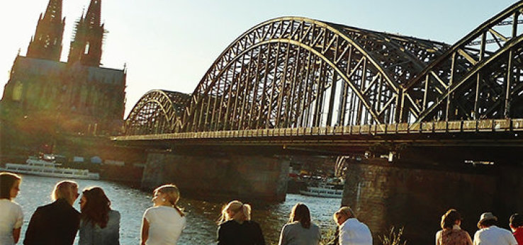 Studierende sitzen am Rhein auf der Deutzer Seite mit Blick auf die Hohenzollernbrücke und den Kölner Dom (Bild: TH Köln / Damir Ahmetovic)