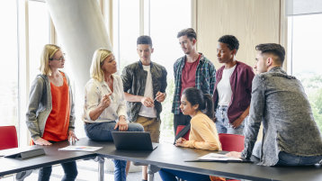 Eine Studienberaterin unterhält sich in locker Atmosphäre mit Schülern*innen im Klassenraum (Bild: istock)