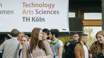 Junge Menschen vor einem Transpararent auf dem "Herzlich willkommen" steht und das Logo der TH Köln (Bild: Costa Belibasakis / TH Köln)