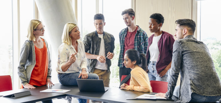 Eine Studienberaterin unterhält sich in locker Atmosphäre mit Schülern*innen im Klassenraum (Bild: istock)