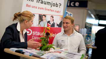 Eine Frau und ein Mann unterhalten sich an einem Messestand (Image: Costa Belibasakis/FH Köln)