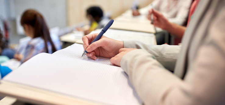 Blick auf Block und Hände eines Studenden in einem Hörsaal. (Bild: TH Köln)