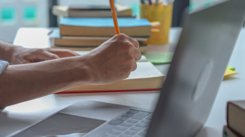 Junger Mann macht sich beim Online-Lernen zu Hause Notizen in einem Notizbuch. (Bild: © Supitnan / Adobe Stock)