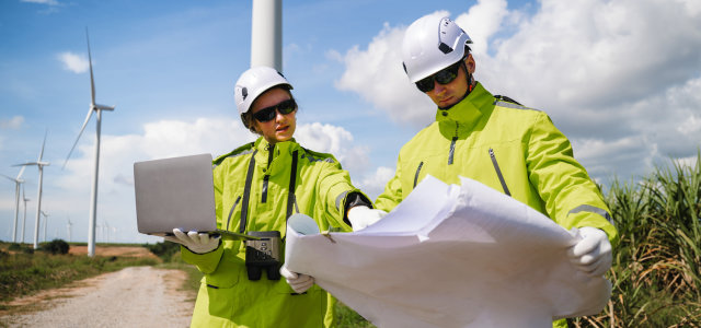 Ein Ingenieur und eine Ingenieurin prüfen Baupläne und digitale Projektdaten vor Ort in einem Windpark (Bild:Adobe Stock/ KL 1981 )