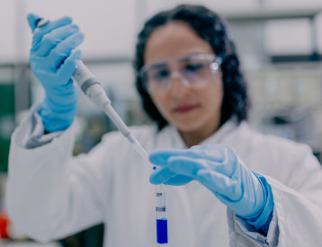 Studierende hält ein Reagenzglas mit blauer Flüssigkeit in einem Labor
