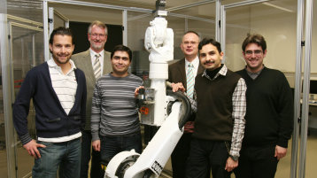 Professoren und ausländische Studierende mit einem weißen Industrieroboter  (Bild: Manfred Stern/FH Köln)
