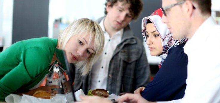 Deutsche und ausländische Studierende schauen in der Mensa auf einen Text auf dem Monitor eines Notebooks  (Bild: Thilo Schmülgen/TH Köln)