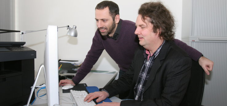Ein Professor sitzt vor einem PC-Bildschirm, ein Student schaut ihm dabei über die Schulter (Bild: Manfred Stern/FH Köln)