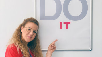 Social Media Managerin Nicole Cuvelier zeigt auf ein Poster mit der Aufschrift "Do it". (Bild: Akademie für wissenschaftliche Weiterbildung TH Köln)