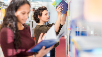 Zwei Frauen bedienen sich an einem Bibliotheksregal. (Bild: TH Köln)