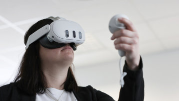 Eine junge Frau trägt eine VR-Brille und hält einen zugehörigen Controller in der Hand. (Bild: TH Köln)