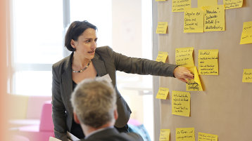 Eine Frau referiert an einer Pinnwand stehend über die daran angeklebten Zettel. (Bild: TH Köln)